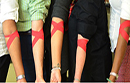 Row of people's arms taped with crossed red IV bandages