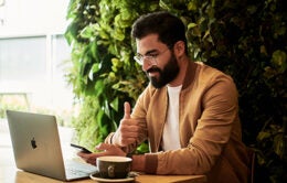 Man working at laptop computer, holding a cellphone