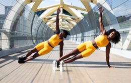 Two women doing side push-ups, wearing yellow workout clothes