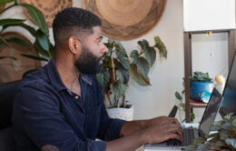 Man working at a computer surrounded by plants and woven hangings