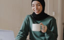 Smiling woman drinking coffee and participating in a video chat on her laptop