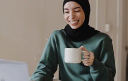 Smiling woman drinking coffee and participating in a video chat on her laptop