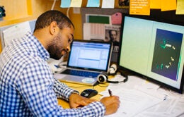 Man working on laptop and with pen and paper