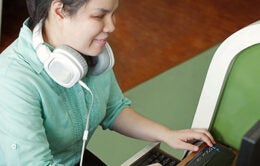 Asian young blind woman with headphone using computer with refreshable braille display or braille terminal a technology device for persons with visual disabilities.