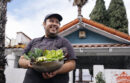 Man holding bowl of freshly-grown lettuces with palm trees in the background