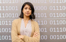 UC student standing in front of a wall of 0s and 1s computer code