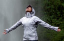Woman wearing a raincoat standing in the spray of a waterfall