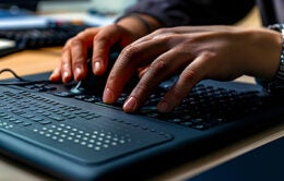 Modern Braille display device connected to a computer, with a visually impaired person using it to read digital text.