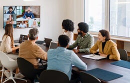 A team actively engages with remote colleagues via a large screen, illustrating the modern hybrid work model where technology bridges the gap between in-office and remote team members