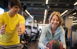 Personal trainer supervising a senior woman exercising at the gym using a medicine ball