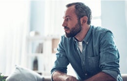 calm bearded middle aged man sitting at home and thoughtfully looking into the distance