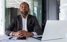 Balanced and calm man at workplace inside office, businessman meditating with closed eyes thinking and visualizing future projects and plans financial strategies, boss inside office with laptop.