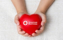 Person holding a red, heart-shaped American Red Cross pillow