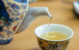 Person pouring tea from a porcelain pot into a teacup