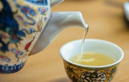 Person pouring tea from a porcelain pot into a teacup