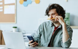 bored looking man looking at a cellphone at his desk