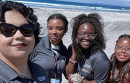 Alesia Andrade, As'Jena Steele, Oluwatolani Olanrewaju Ojo and Breanna Holifield standing on the beach in the sun