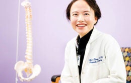 Patricia Zheng sitting by a skeletal model of a spine in her office