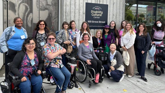 Group of people standing or sitting in wheelchairs together in front of the SF Disability Cultural Center