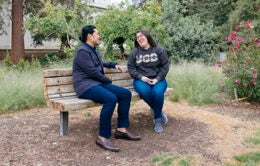 Two people talking on a bench outside