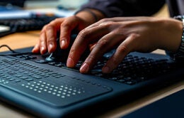 Modern Braille display device connected to a computer, with a visually impaired person using it to read digital text.