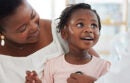 Parent holds child while a doctor listens to her heart with a stethoscope.