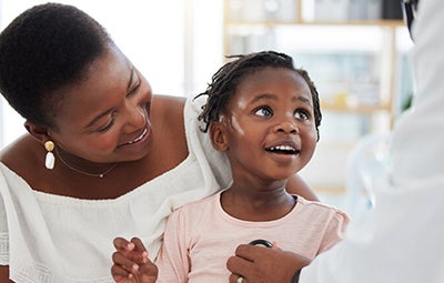 Parent holds child while a doctor listens to her heart with a stethoscope.