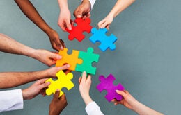 High Angle View Of Medical Team Solving Colorful Jigsaw Puzzle Against Grey Background