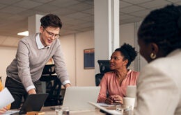 A group of colleagues cooperating and brainstorming around a table in a contemporary professional office environment.