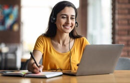 Happy young woman having educational course online, using laptop and headset