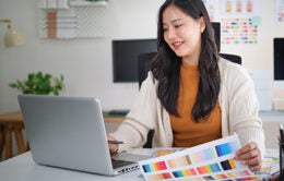 Female web designer developing mobile app layout, reviewing user interface mockups and design plans.