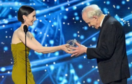 Woman handing a man a trophy on a brightly lit stage