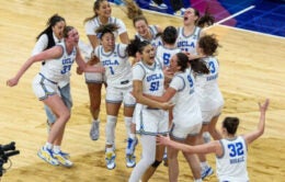 UCLA women's basketball team members come together on the court to celebrate their victory