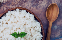 Wooden bowl of sticky rice with basil leaves on top next to a wooden spoon
