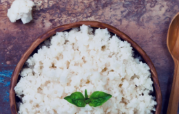 Wooden bowl of sticky rice with basil leaves on top next to a wooden spoon