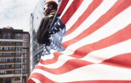Man standing in the wind with an American flag wrapped around him