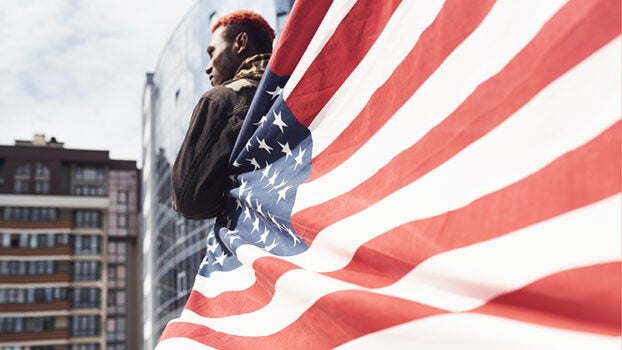 Man standing in the wind with an American flag wrapped around him