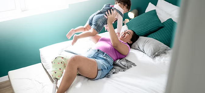 Mom with artificial limb holding baby in the air while lying on her bed