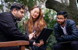 UC students looking at an iPad while sitting in a wooded area
