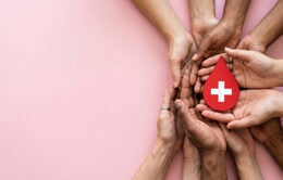 Multiple hands holding a red paper blood droplet with a white cross