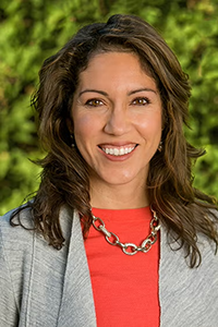 Maria Anguiano, smiling in a gray suit and red shirt