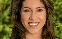 Maria Anguiano, smiling in a gray suit and red shirt
