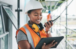 Tablet, engineer and black woman worker planning on a construction site strategy and talking on a walkie talkie. Project management, infrastructure and female contractor doing building assessment.