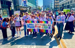 UCOP Pride members pose on the street in Oakland holding a banner that reads "Let There Be Pride"