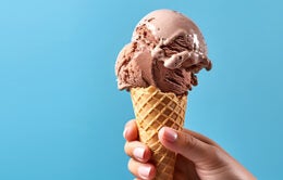 Hand holding chocolate ice cream cone on blue background.