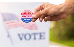 Hand showing I voted today badge at ballot box at American elections.